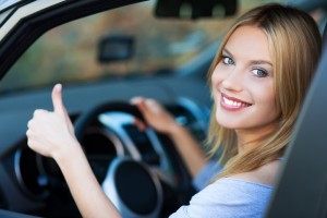 Uśmiechnięta blondynka pokazująca kciuk do góry za kierownicą w samochodzie